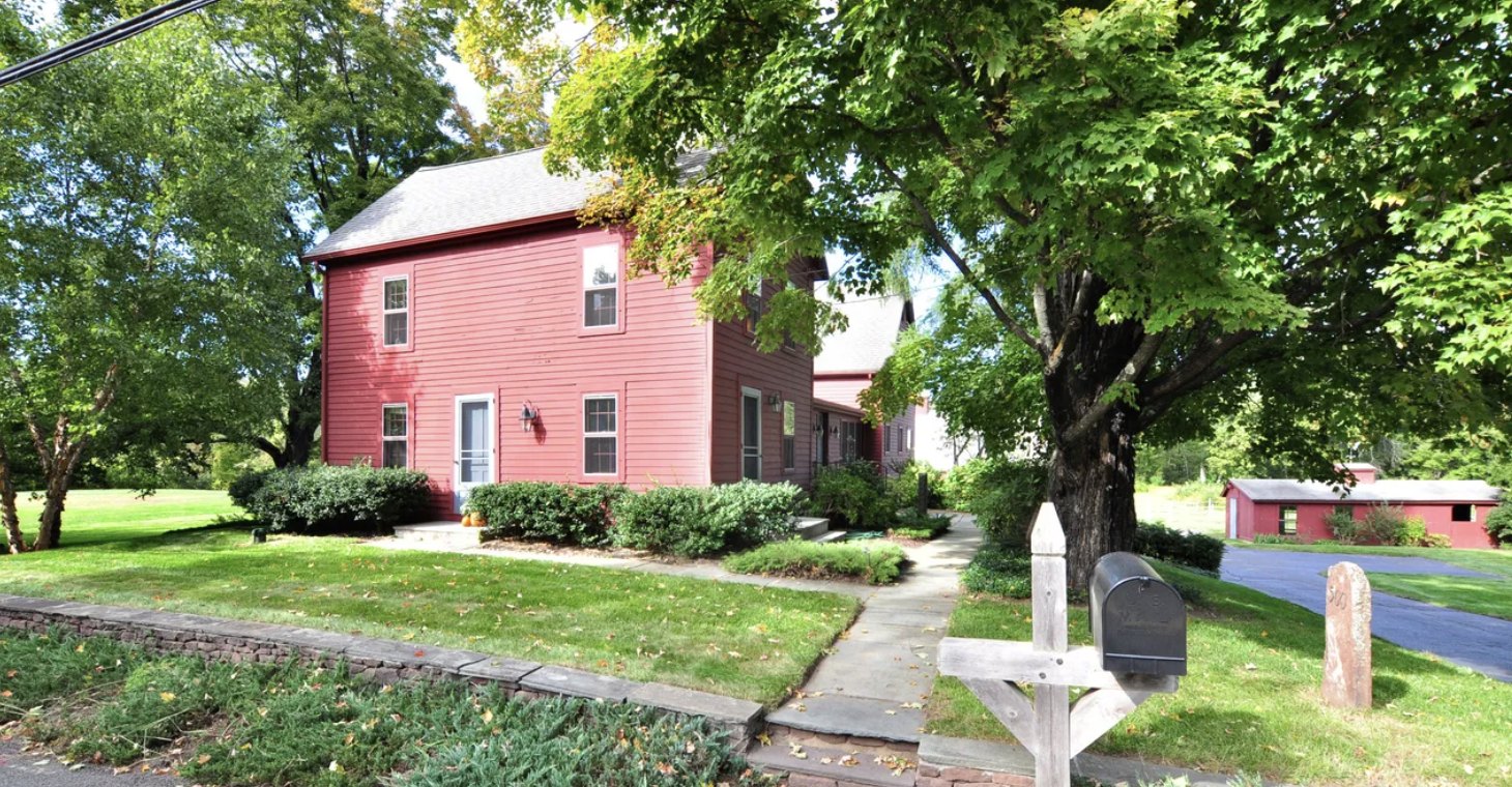 Red clapboard farmhouse built in 1862 with a side ell and detached outbuilding under a mature maple in Simsbury CT