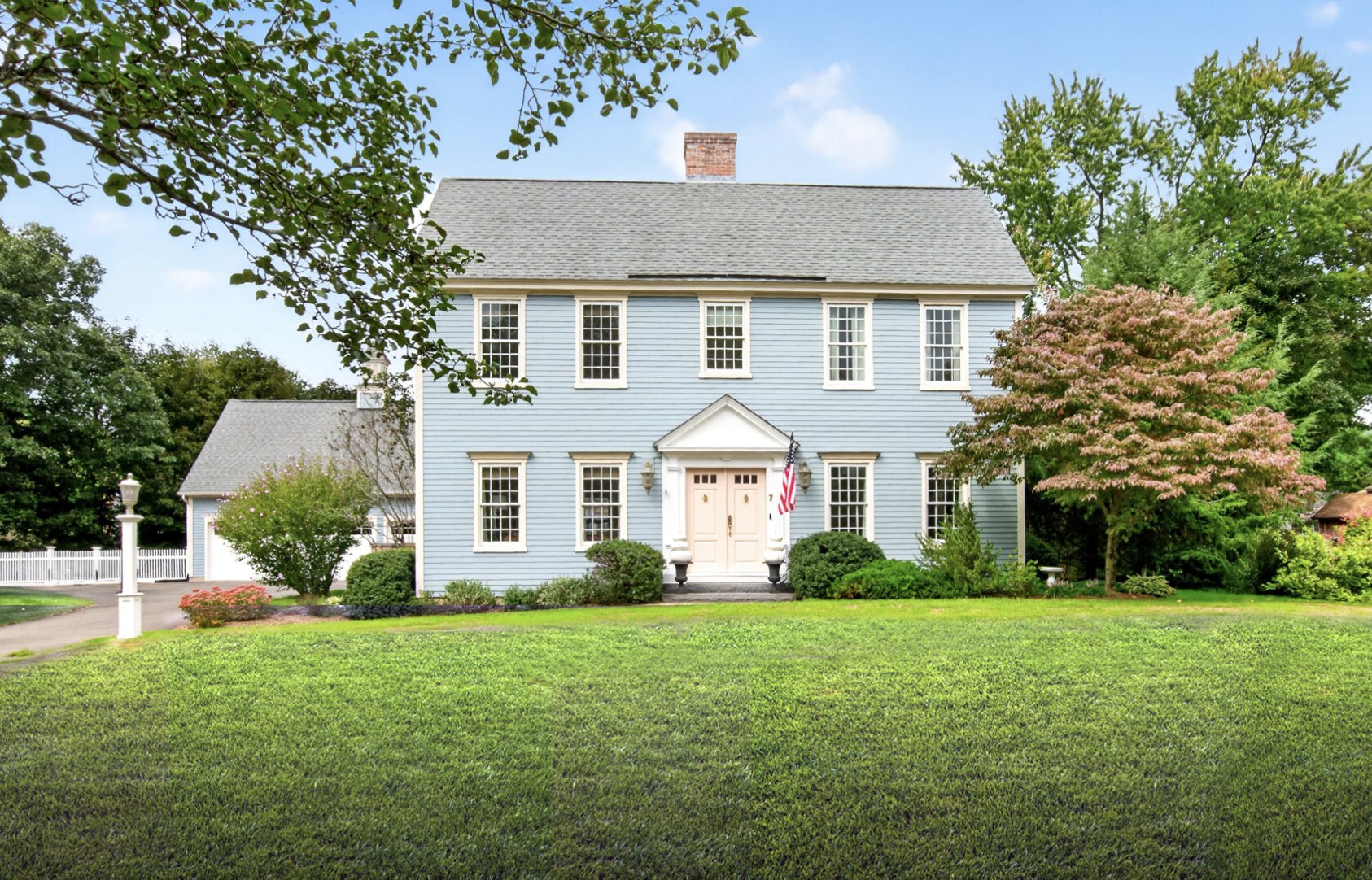 Two-story light blue colonial style home with white trim, a pedimented double front door, an attached garage, and a front lawn in Simsbury CT